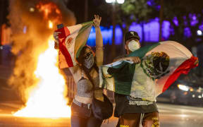Protesters hold up Mexican flags amid clashes with law enforcement in the streets surrounding the federal building during a protest following federal immigration operations in Los Angeles, California, on June 8, 2025. Demonstrators torched cars and scuffled with security forces in Los Angeles on June 8, as police kept protestors away from the National Guard troops President Donald Trump sent to the streets of the second biggest US city. (Photo by RINGO CHIU / AFP)