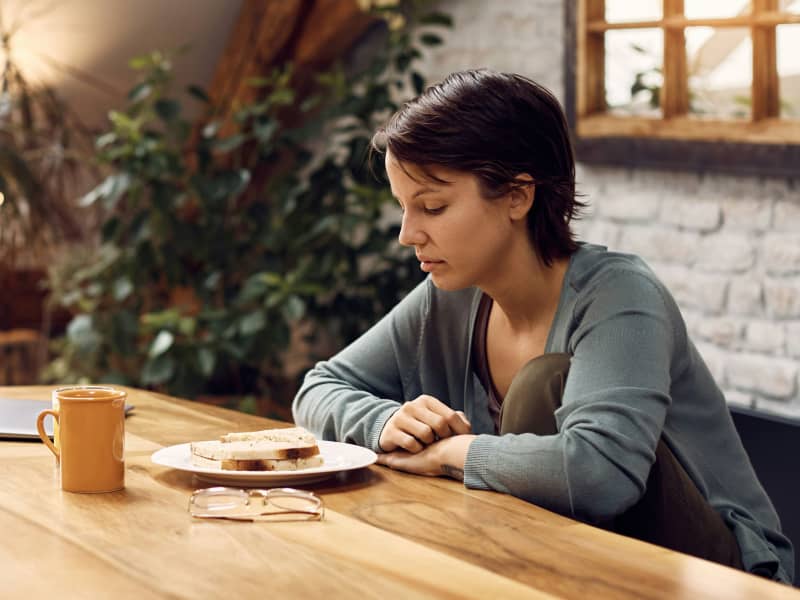 A woman with short dark hair looks down at a sandwich.