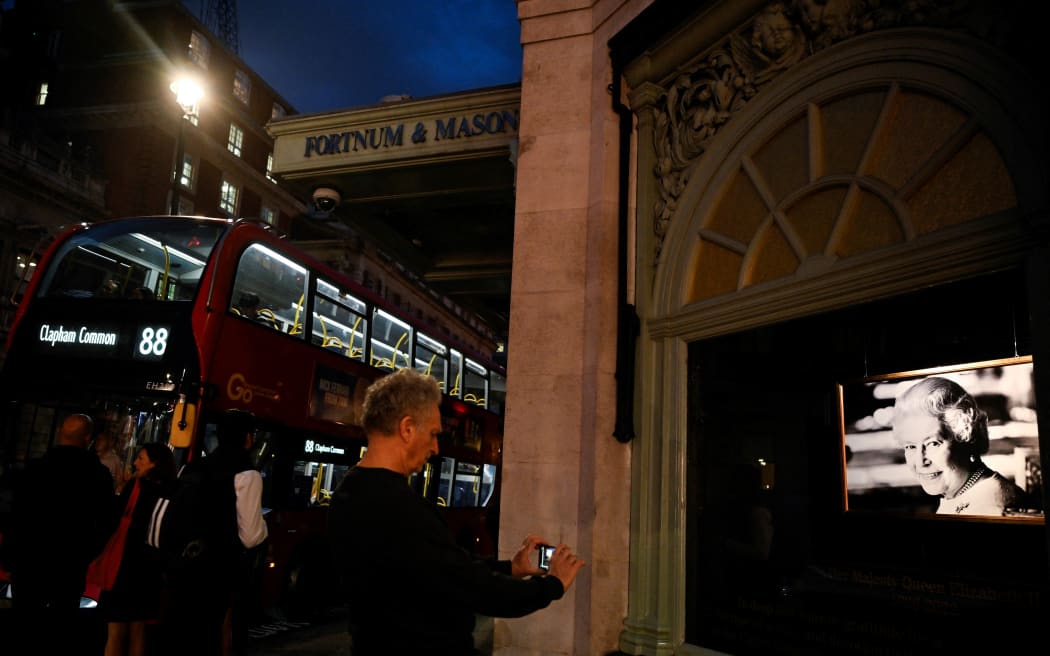 A pedestrian takes a picture of a photograph of late Queen Elizabeth II displayed as a tribute outside Fortnum and Mason shop, in central London on September 15, 2022, following the death of her Majesty on September 8. - Queen Elizabeth II will lie in state until 0530 GMT on September 19, a few hours before her funeral, with huge queues expected to file past her coffin to pay their respects. (Photo by Louisa Gouliamaki / AFP)