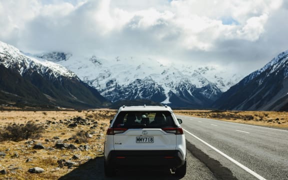 A car on the road in the South Island, with snowy peaks ahead.