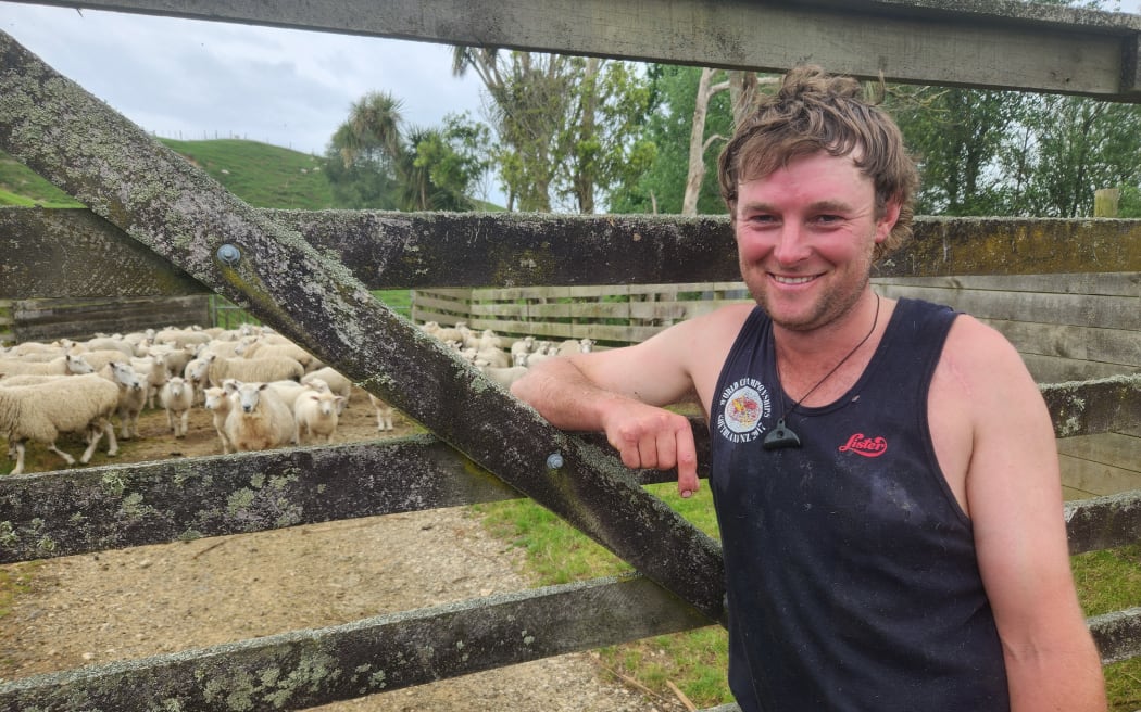 Mitchel Hoare in shearing singlet leaning on farm gate with sheep in background