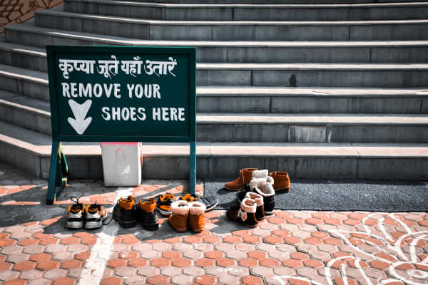 A sign in English and Hindi, asking people to remove their shoes before entering, with several pairs of shoes left next to it.