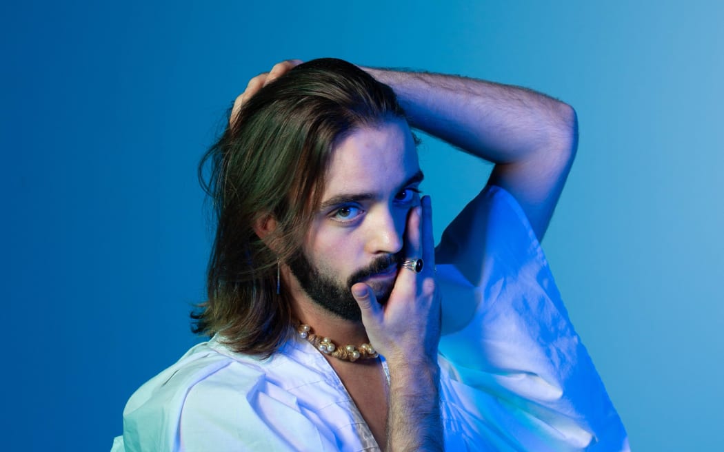 A man wearing a white shirt poses in blue light in front of a blue screen.