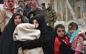 Syrian residents fleeing the eastern part of Aleppo walk through a street in Masaken Hanano, a former rebel-held district which was retaken by the regime forces last week, on November 30, 2016.
