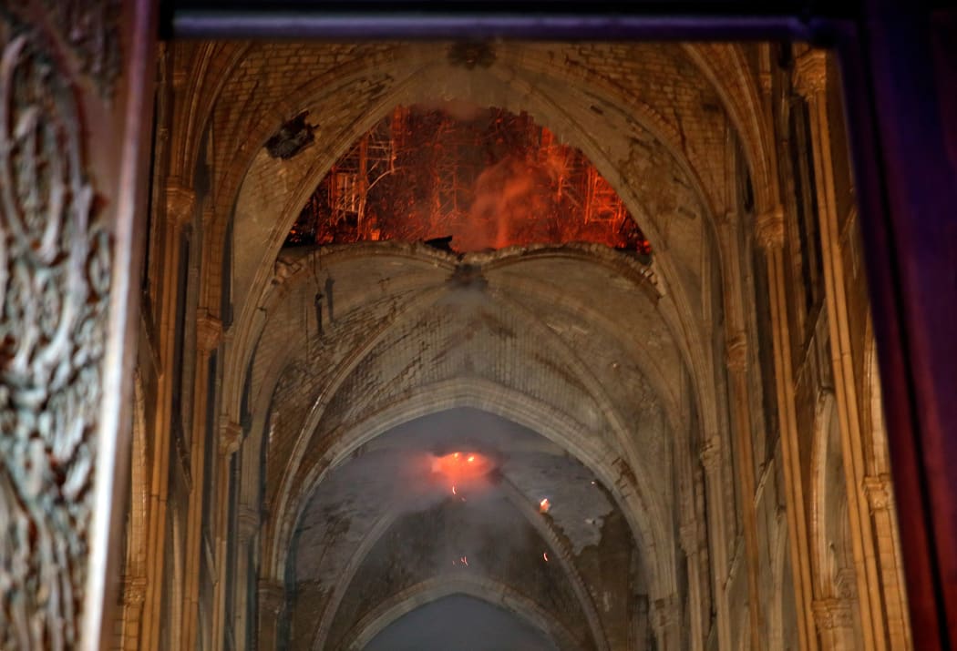 Stone vaults inside Notre-Dame Cathedral with flames are seen through the damaged roof.