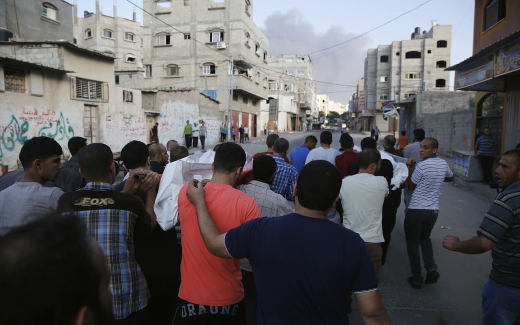 Palestinians carry the bodies of two men as smoke rises over Beit Lahiya in the northern Gaza Strip.