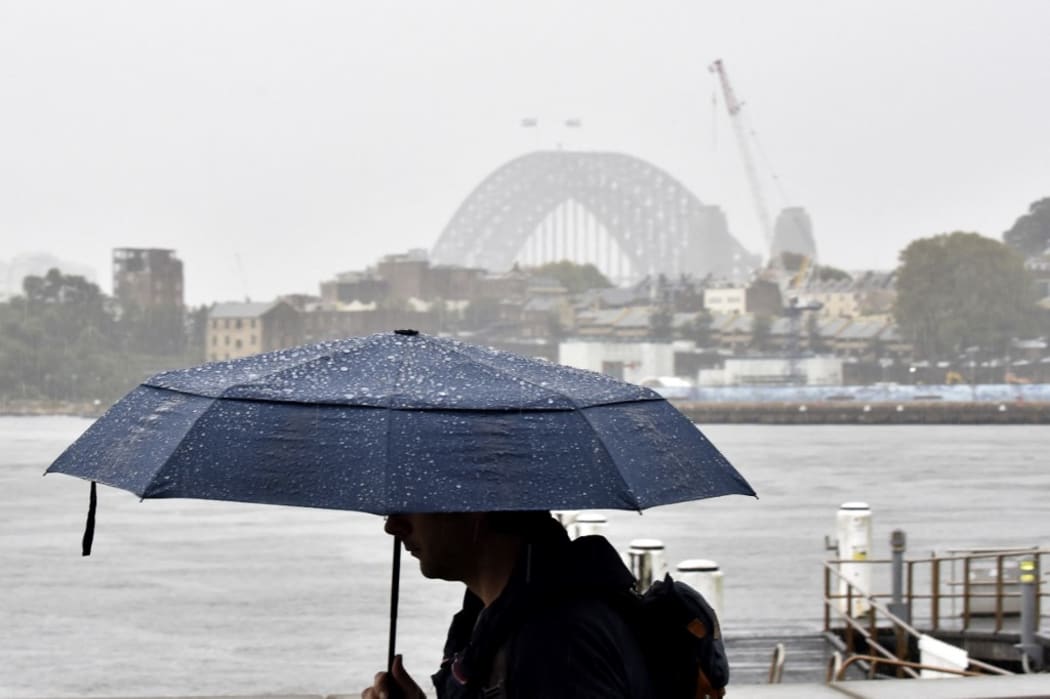 A man walks in front of the Harbour Bridge during rainfall in Sydney on 7 April as inclement weather triggered evacuation orders in several suburbs of Sydney's south and southwest.