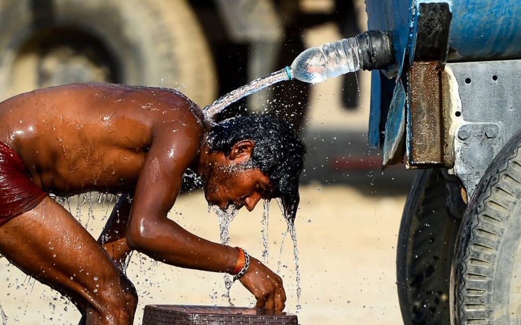 (FILES) In this file photo taken on May 31, 2019, an Indian truck driver takes a bath using a water tanker as he tries to cool himself on a hot summer afternoon in Allahabad.
