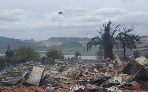 A monsoon helicopter flies over the remains of a house razed by a scrub fire near Whitianga. At least four houses and several other buildings have burnt to the ground.