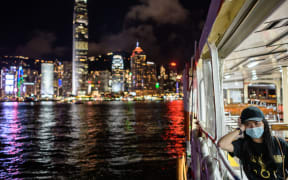 A woman on a passenger ferry in Victoria Harbour travelling away from Kowloon to Hong Kong Island