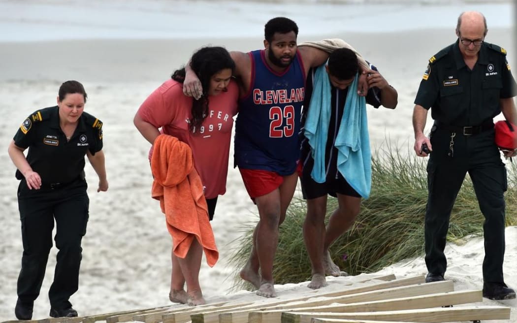 Lua Rasmussen (second left) helps Mosese Dolodolotawake (centre) ashore after the pair were among four friends caught in a rip last night.