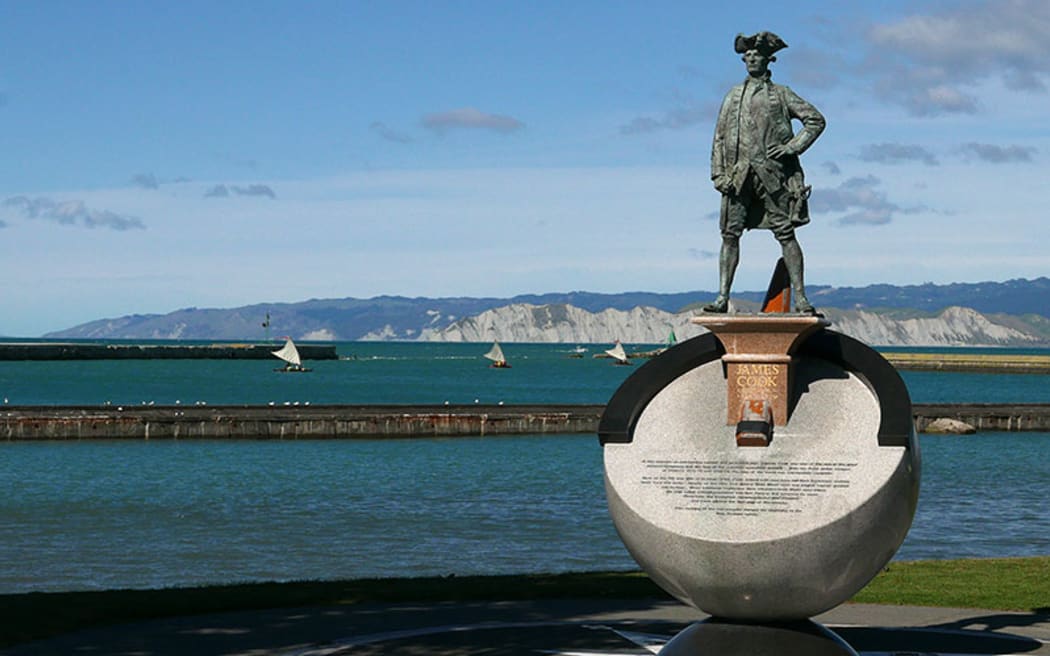 Cook and Vaka - a flotilla of sailing va'a cruise offshore of a statue of James Cook on the Gisborne foreshore