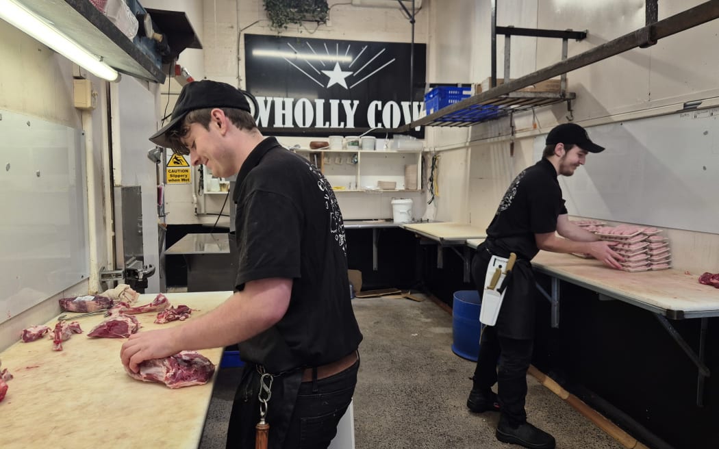 A pair of butchers packing sausages and deboning a leg of lamb.