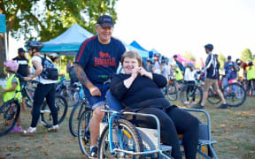 A man riding a bike with a woman in a wheelchair attached to the front.