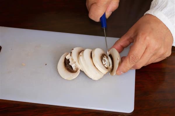 A person chops mushrooms on a plastic board.