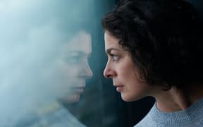 woman with black here looking out a window with reflection