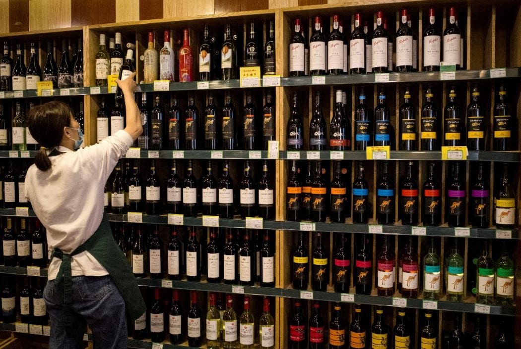 An employee works as Australian-made wine (on display shelves on R) are seen for sale at a store in Beijing on August 18, 2020. -
