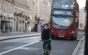 A man wearing a face mask as a preventive measure against the coronavirus (Covid-19) pandemic rides his bike in central London, England on May 5, 2020.