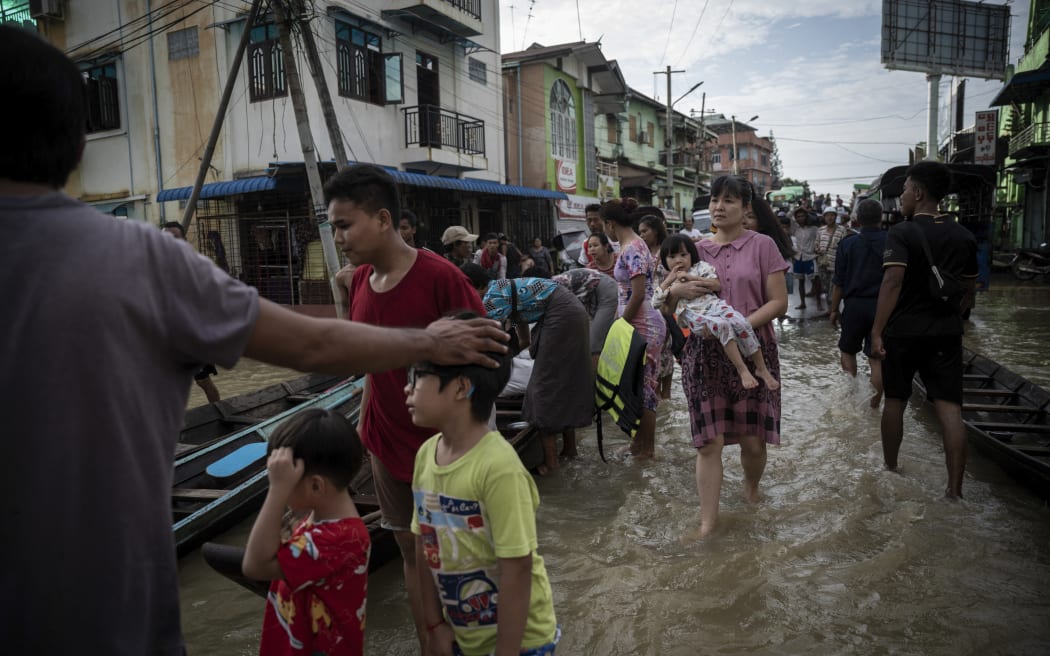 Residents wade through a flooded street following monsoon rains in Bago township, Bago region, on August 11, 2023. Floods and landslides caused by monsoon rains have killed five people and forced the evacuation of around 40,000 others in Myanmar, officials said on August 11. (Photo by Sai Aung Main / AFP)