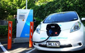 An a white electric car with a black cable running into the bonnet at a charging station, Dunedin