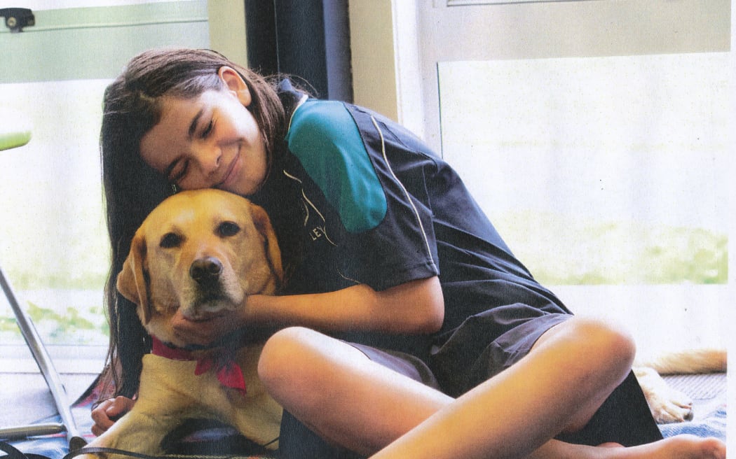 Greta lies on a blanket in a library. A young girl cuddles Greta, smiling.
