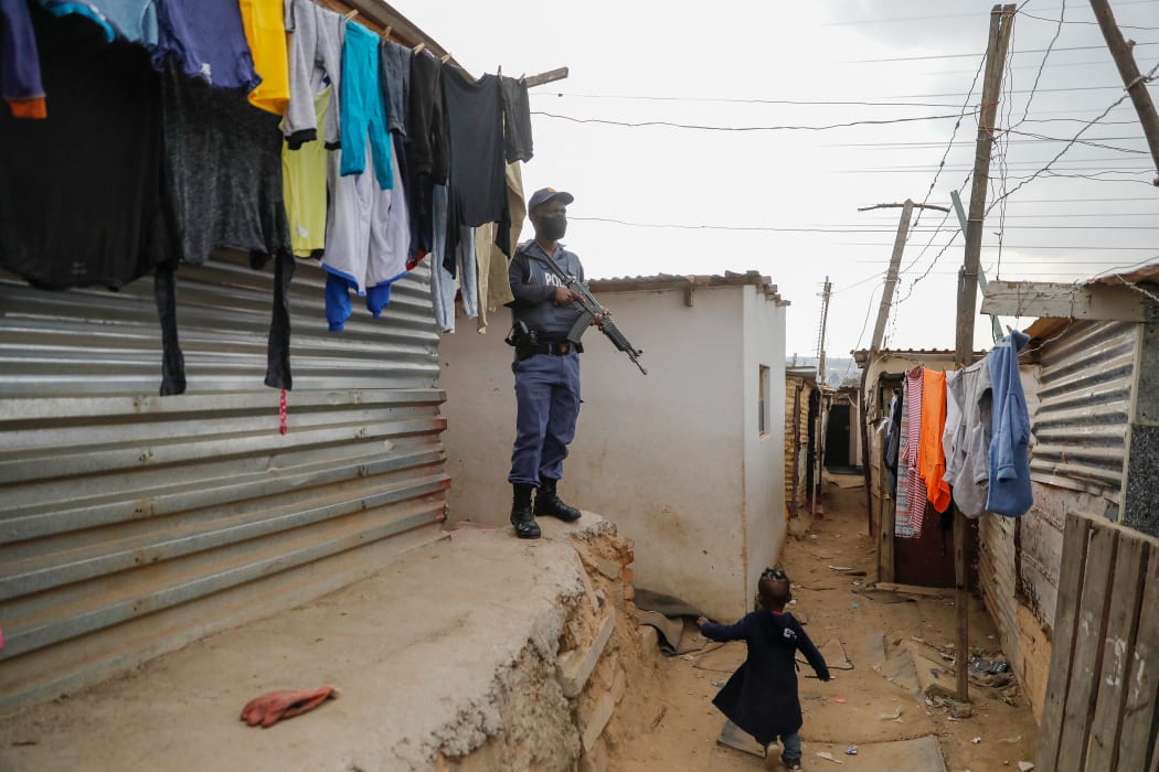A child runs past a member of the South African Police Services (SAPS) while keeping watch during a joint operation with South African Defence Force (SANDF) to recover stolen goods from the looting in Alexandra township, Johannesburg, on July 16, 2021. -