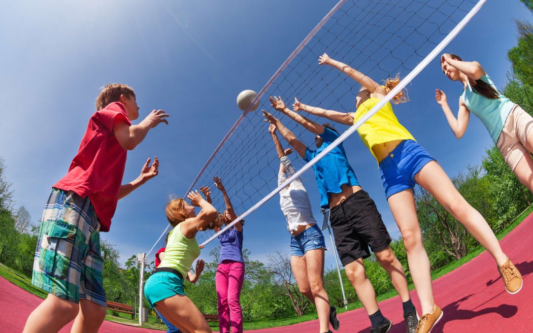 Teenagers playing volleyball together outside on a sunny day.