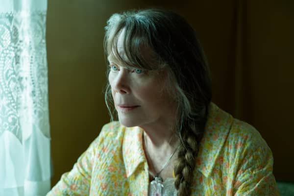 Sissy Spacek, wearing a yellow shirt, looks across the room with concern.