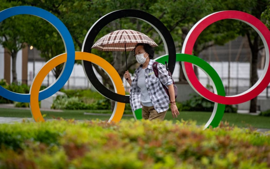 A woman holds an umbrella walking past the Olympic Rings in front of Japan Olympic Museum in Tokyo on July 8, 2021. (Photo by Philip FONG / AFP)