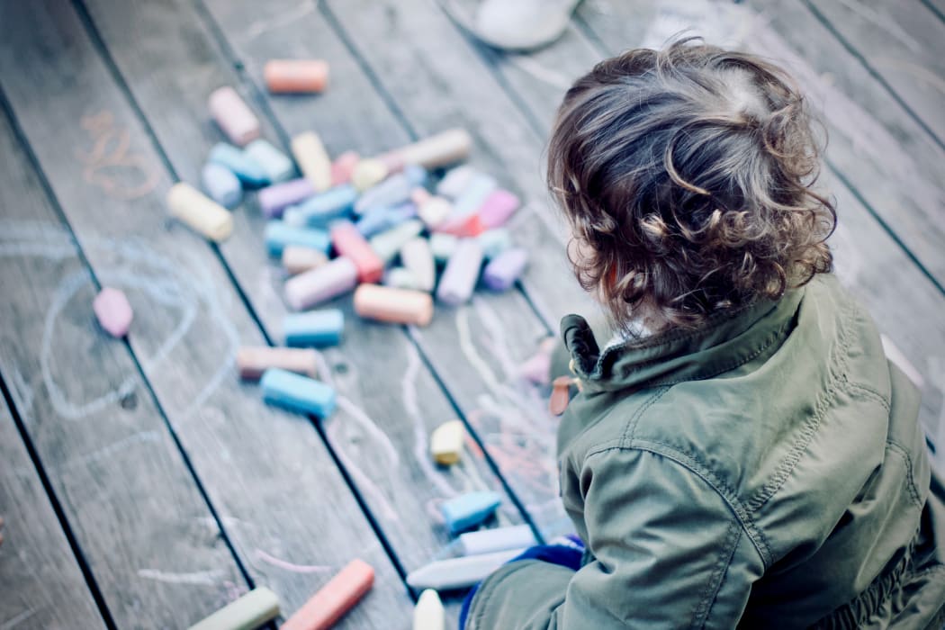 Child sitting on floor playing with chalks.