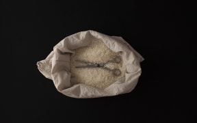 A pair of surgical scissors lying flatly on the top of a bag of rice.