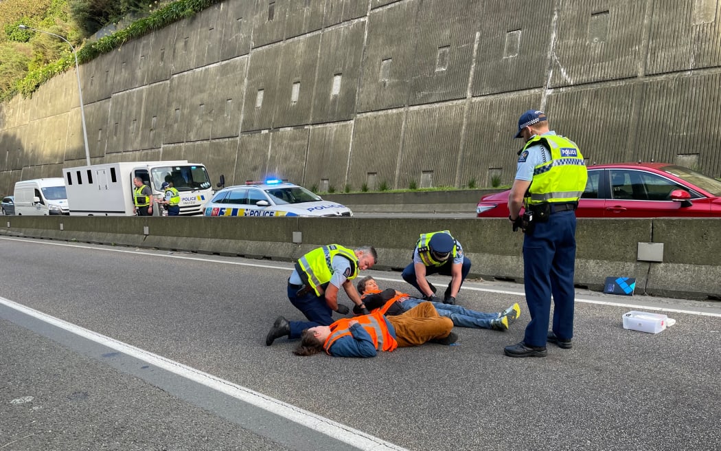Police removing two protesters who glued their hands to the soutbound lanes of the motorway at the Terrace Tunnel, Wellington.
