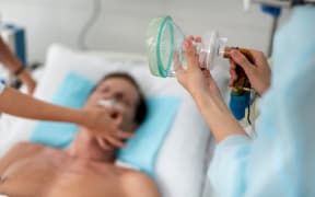 Man lying in hospital bed, medical worker's hand holding respiratory equipment.