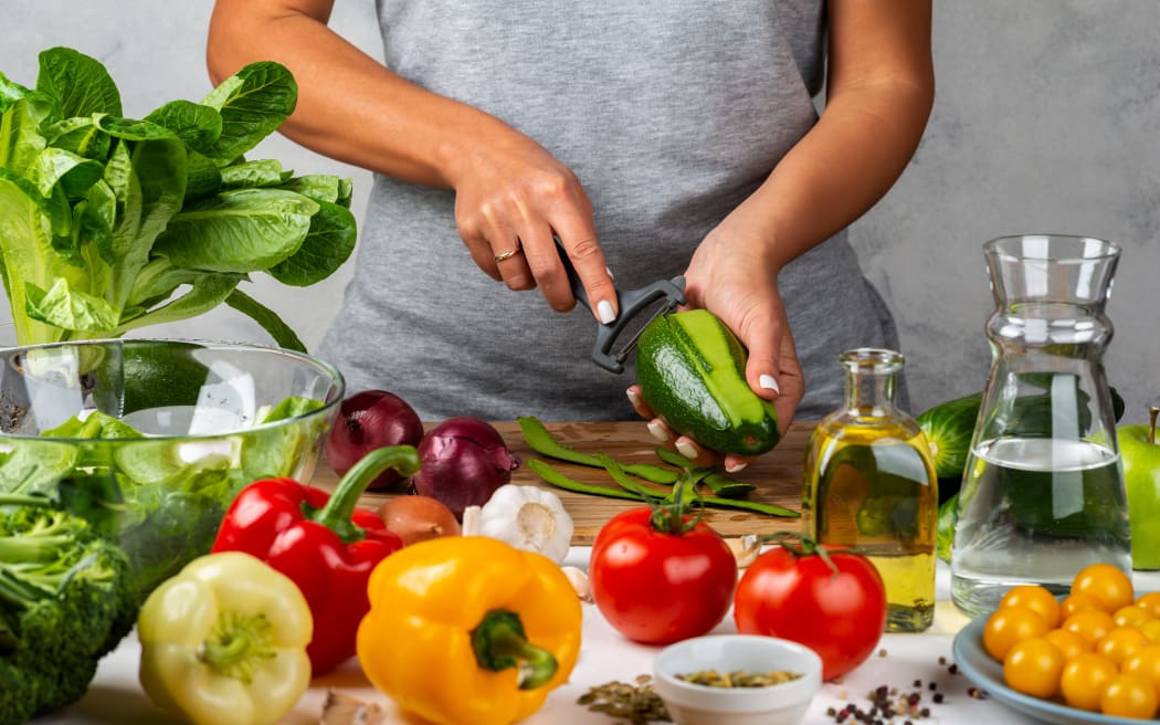 Woman is peeling avocado, cooking salad in the kitchen. Healthy diet concept