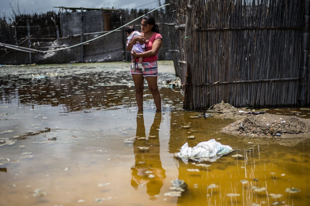A woman and her baby stand in a flooded street in the province of La Union in Piura, northern Peru, on March 25, 2017. The El Nino climate phenomenon is causing muddy rivers to overflow along the entire Peruvian coast, isolating communities and neighbourhoods.