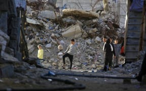 Palestinian children watch as another plays with a football next to the rubble of destroyed buildings by the Israeli military in Khan Yunis in the southern Gaza Strip on January 27, 2026. Since October 10, a fragile US-sponsored truce in Gaza has largely halted the fighting between Israeli forces and Hamas, but both sides have alleged frequent violations.