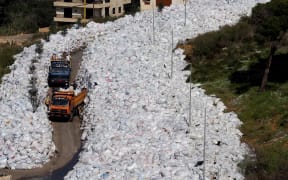 Rubbish trucks drive between a built up pile of waste on a street in Beirut's northern suburb of Jdeideh on February 25, 2016
