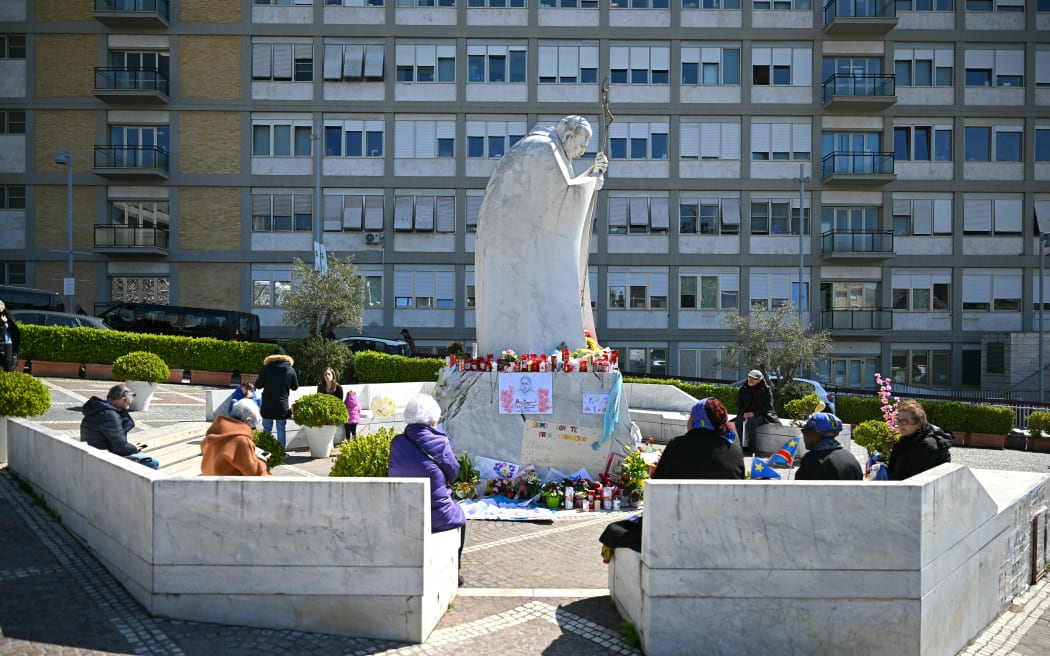 People sit around the statue of Pope John Paul II outside the Gemelli Hospital where Pope Francis is hospitalised with pneumonia, in Rome, on 20 March, 2025.