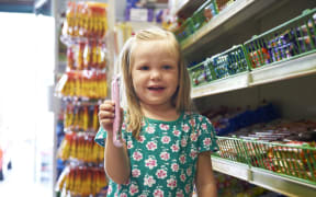 A little girl with a big smile stands next to the lolly aisle at a supermarket (file)