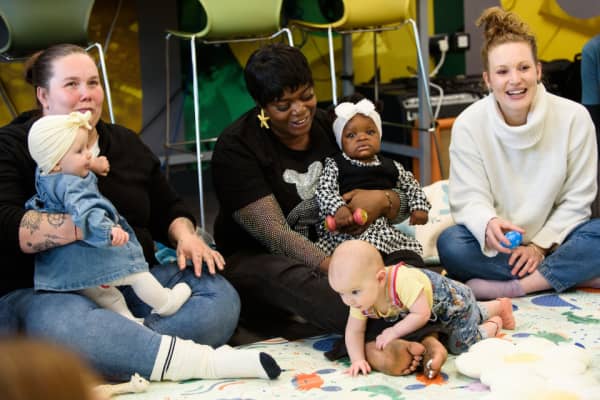 Three mums sitting on the floor hold their babies and smile.