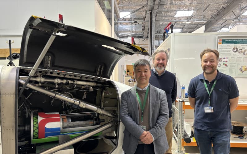 The three men stand next to an airplane part that's been opened on one side to show a model of what they are trying to accomplish - an electric motor to drive the propeller.
