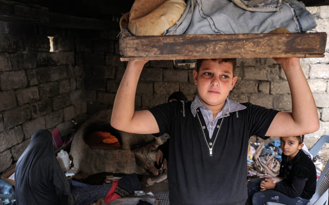 A young man carries a tray of freshly baked bread from a clay oven outside a home in Khan Yunis in the southern Gaza Strip on November 9, 2023 amid continuing battles between Israel and the Palestinian militant group Hamas. (Photo by MOHAMMED ABED / AFP)