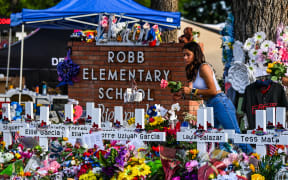 (FILES) A girl lays flowers at a makeshift memorial at Robb Elementary School in Uvalde, Texas, on May 28, 2022. Relatives of children killed or wounded by a mass shooter in Uvalde two years ago have reached a $2 million settlement with the Texas city, a lawyer for the families said May 22, 2024. Nineteen small children and two teachers were killed when a teenage gunman went on a rampage at Robb Elementary School in May 2022 in America's worst school shooting in a decade. (Photo by CHANDAN KHANNA / AFP)