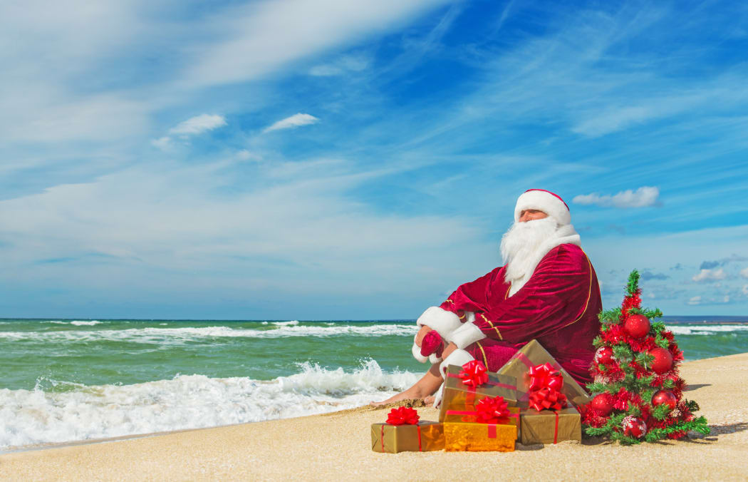 Santa Claus at sea beach with many gifts and decorated christmas tree - happy new year concept