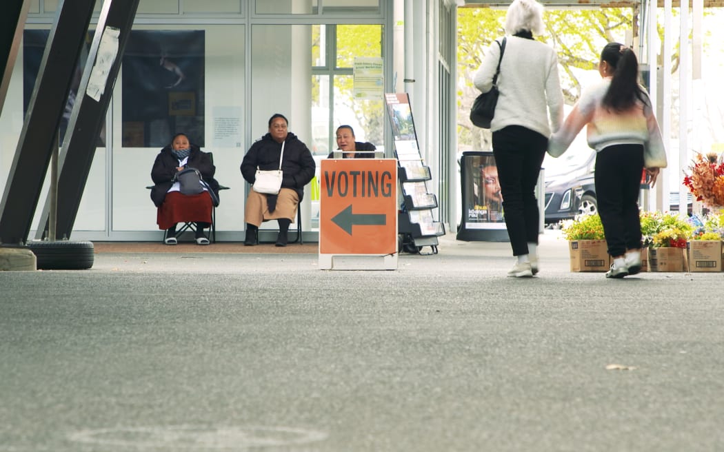 People sit behind a voting sign while others walk towards it in South Auckland.