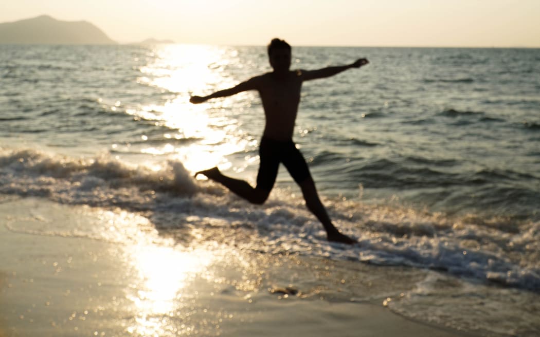 Silhouette of a man jumping on the beach at sunset.