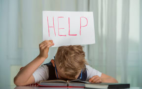 Kid boy sleeping with a textbook over his head and holding a sign with the word Help