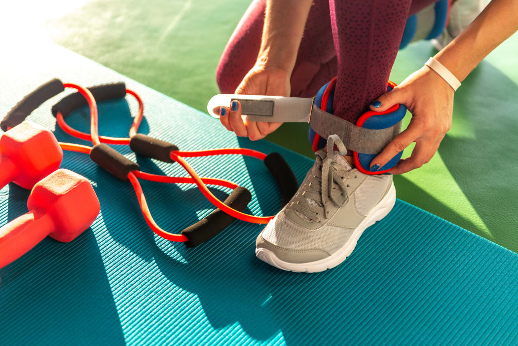 Woman putting on ankle wights before she starts a workout in a gym.