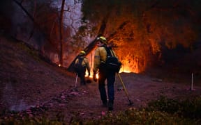 Firefighters work to put out flames in the Mandeville Canyon neighborhood of Los Angeles, California, on January 11, 2025, as the Palisades Fire continues to burn. The Palisades Fire, the largest of the Los Angeles fires, spread toward previously untouched neighborhoods January 11, forcing new evacuations and dimming hopes that the disaster was coming under control. Across the city, at least 16 people have died as multiple fires have ripped through residential areas since January 7, razing thousands of homes in destruction that US President Joe Biden likened to a "war scene." (Photo by AGUSTIN PAULLIER / AFP)