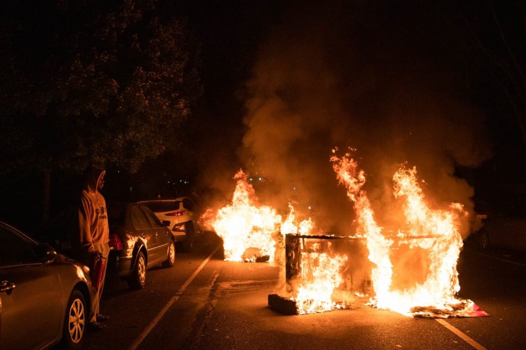 A man watches as a sofa, set on fire by protesters, burns in his street in West Philadelphia on October 27, 2020,  during a demonstration against the fatal shooting of 27-year-old Walter Wallace, a Black man, by police.